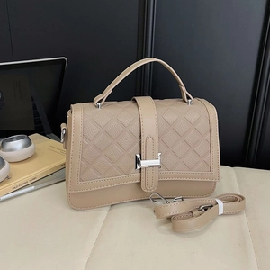 Quilted beige crossbody handbag with silver H-buckle and adjustable strap on a sofa