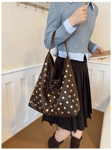 Detailed close-up of large brown tote bag with retro silver rivets on matte leather