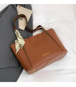 Dettaglio di una borsa tote marrone motivo litchi con scritte dorate e foulard in seta