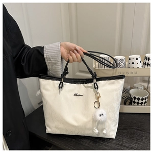 Detail of white tote bag with textured canvas, black handles, and plush keychain charm