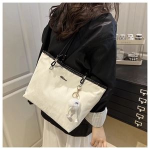 Minimalist white tote bag with black leather straps and plush monster charm on model