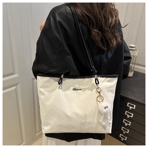 Shoulder view of white tote bag with black handles and plush charm accessory
