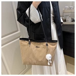 Detail of khaki tote bag featuring pleated texture, metal logo and plush charm accessory
