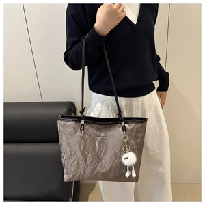Détail d'un sac cabas gris avec texture plissée et porte-clés en peluche blanche élégant
