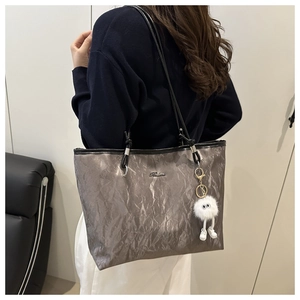 Silver wrinkled tote bag with black strap and white plush charm on model shoulder