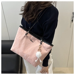 Detailed side view of pink tote bag with thin black straps and white fluffy pom-pom charm