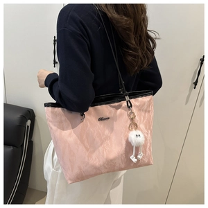 Détail d'un cabas rose plissé avec logo en métal et breloque en peluche sur la bandoulière
