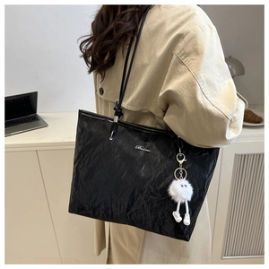 Detail of black tote bag with glossy wrinkled texture and white fuzzy ball charm