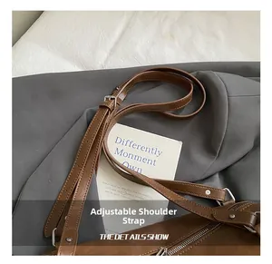 Détail d'une bandoulière réglable en cuir marron avec boucle en métal et rivet
