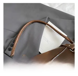 Détail d'un sac à bandoulière en cuir marron avec poignées lisses et fermeture éclair