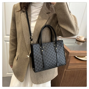 Detail of a chic tote bag with M-pattern monogram and adjustable strap on a female model