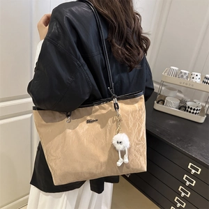 Retro khaki pleated tote bag with black straps and plush monster charm on a model