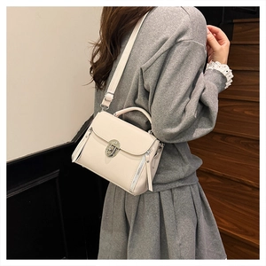 Detail of ivory leather handbag with silver twist lock and side zipper tassels worn on shoulder
