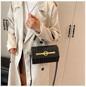 Detail of black woven texture handbag with metal M-logo buckle worn with beige coat