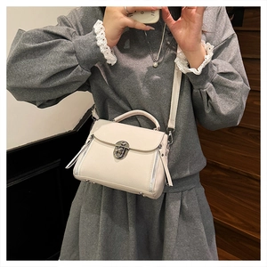Detail of cream white textured crossbody bag with silver buckle and tassel accents