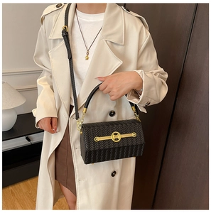 Detail of black woven texture handbag with golden M-logo clasp shown on cross-body strap