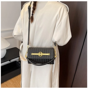 Detail of a black woven texture crossbody bag with gold M-buckle on a beige trench coat