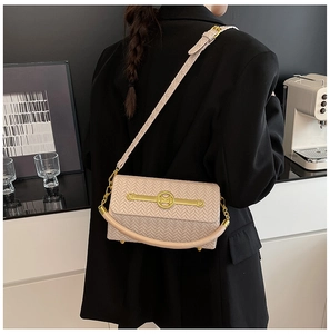 Detail view of beige crossbody bag with woven texture and gold M-logo buckle on model