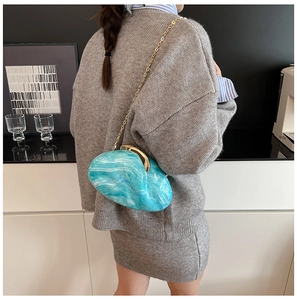 Blue marble acrylic evening bag with gold chain strap worn by a model in a modern room