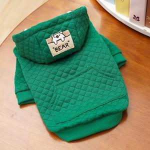 Detailansicht eines grünen gesteppten Haustier-Hoodies mit Bären-Patch und Tasche auf Holz