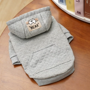 Detail eines grauen gesteppten Haustier-Hoodies mit Bären-Abzeichen auf Holzgrund