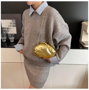 Close-up of irregular gold metallic evening bag with chain strap on grey knit outfit