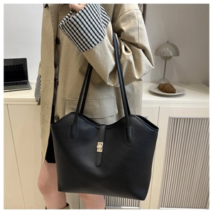 Detail of large black pebbled leather tote bag with gold metal clasp on a lifestyle model