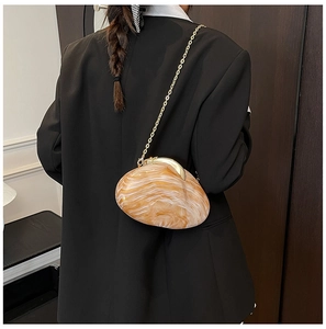 Detailed view of amber marble acrylic shell bag with gold chain strap on black blazer