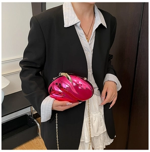 Close-up of fuchsia metallic clutch bag with gold chain strap on stylish black outfit