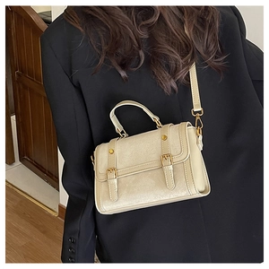 Détail d'un sac Boston vintage beige avec clous dorés sur une veste de blazer noire
