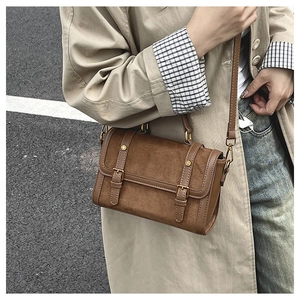 Gros plan d'un sac cartable vintage marron porté avec un trench-coat beige élégant