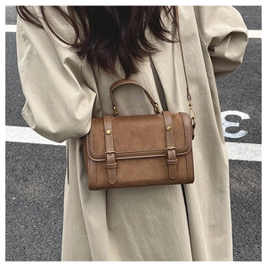 Sac bandoulière vintage marron mat avec boucle dorée porté sur un trench-coat classique