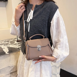 Brown leather crossbody bag with metal lock and decorative zippers shown on a model