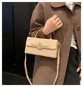 Close-up of beige crossbody box bag with golden M logo and spiral metal handle on a model