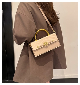 Detail of beige box bag with golden bamboo handle and M-logo buckle on brown coat
