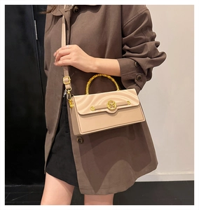 Detail of beige box bag featuring a golden bamboo handle and textured wavy flap
