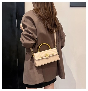 Detail of elegant beige crossbody bag with gold spiral handle and M logo on brown blazer