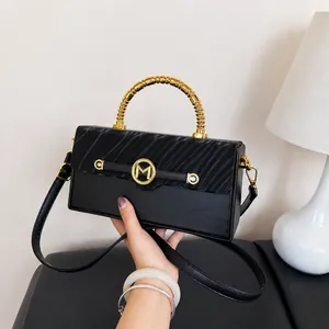 Detail of black faux leather box bag featuring golden spiral handle and M logo hardware