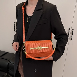 Orange woven crossbody box bag with gold M-logo buckle worn by model in black suit