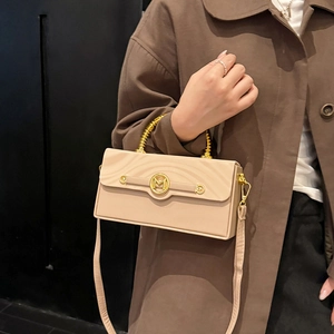 Beige rectangular box bag with gold spiral handle and M-logo, shown on a brown coat