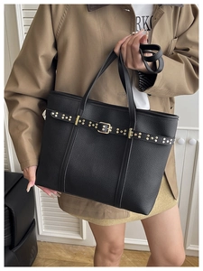 Detail of black pebbled leather tote bag with gold rivets and metallic buckle accents