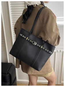 Close-up of black lychee leather tote bag with gold rivet belt detail on female model