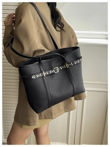 Detail of black pebbled leather tote bag with gold rivets and long shoulder strap