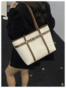 Detail of a cream bucket tote bag with brown straps and pebble leather texture on model