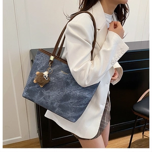 Détail d'un sac cabas bleu texturé avec bandoulière marron et pendentif peluche