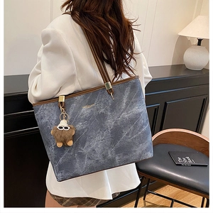 Détail du cabas en denim bleu avec lanières en cuir marron et breloque monstre en peluche
