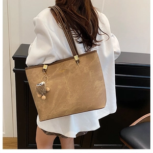 Détail du sac cabas vintage en cuir marron avec pompon décoratif et texture élégante