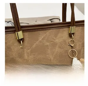 Détail du cabas marron rétro avec logo doré embossé et charm de monstre mignon attaché