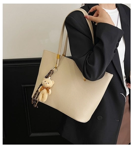 Detail of off-white lychee pattern tote bag with cute brown teddy bear charm accessory