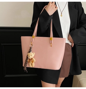 Close-up of light pink tote bag with bear charm and scarf on textured faux leather